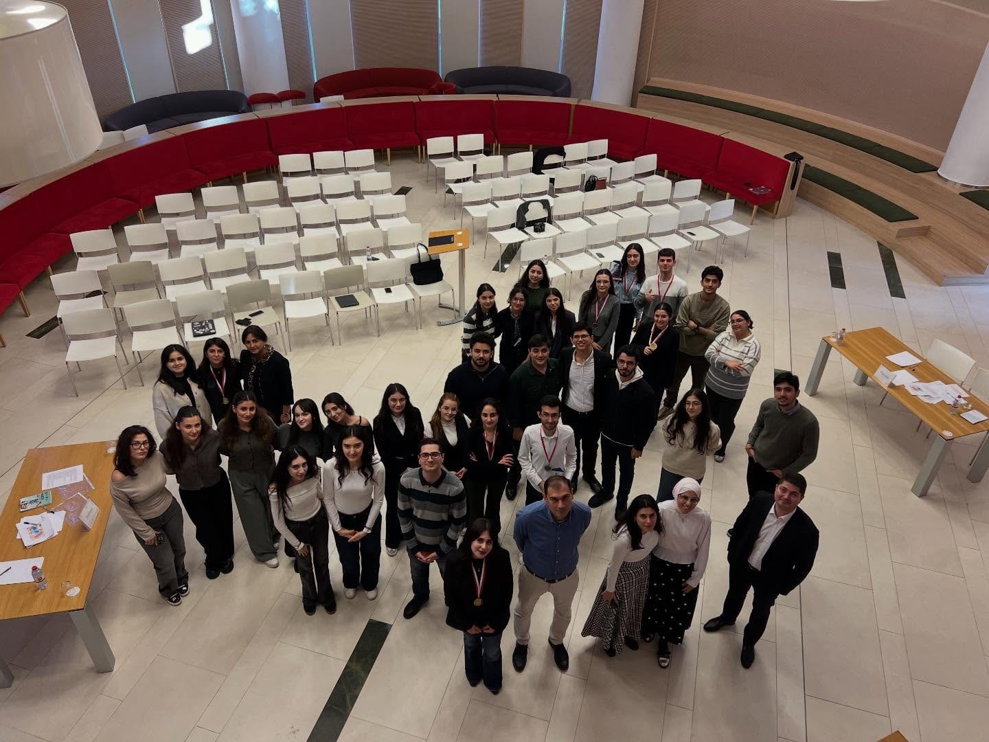 Participants, judges and organisers of the debate tournament gathered for a group photograph in a large atrium, rows of white chairs behind them.